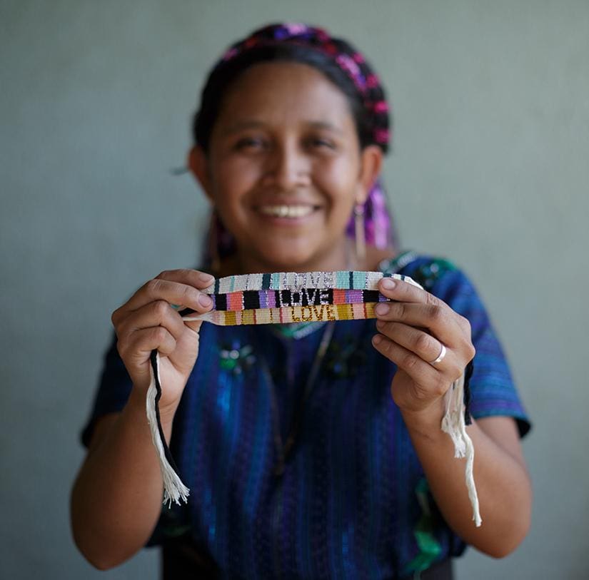 An artisan holds a Green and White Atitlan LOVE Bracelet from Love Is Project
