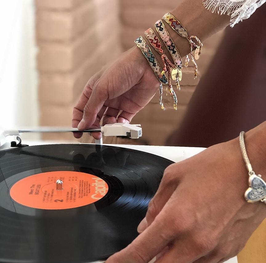 A model holding a vinyl record wearing the Desert Bali Friendship Bracelet Bundle from Love Is Project